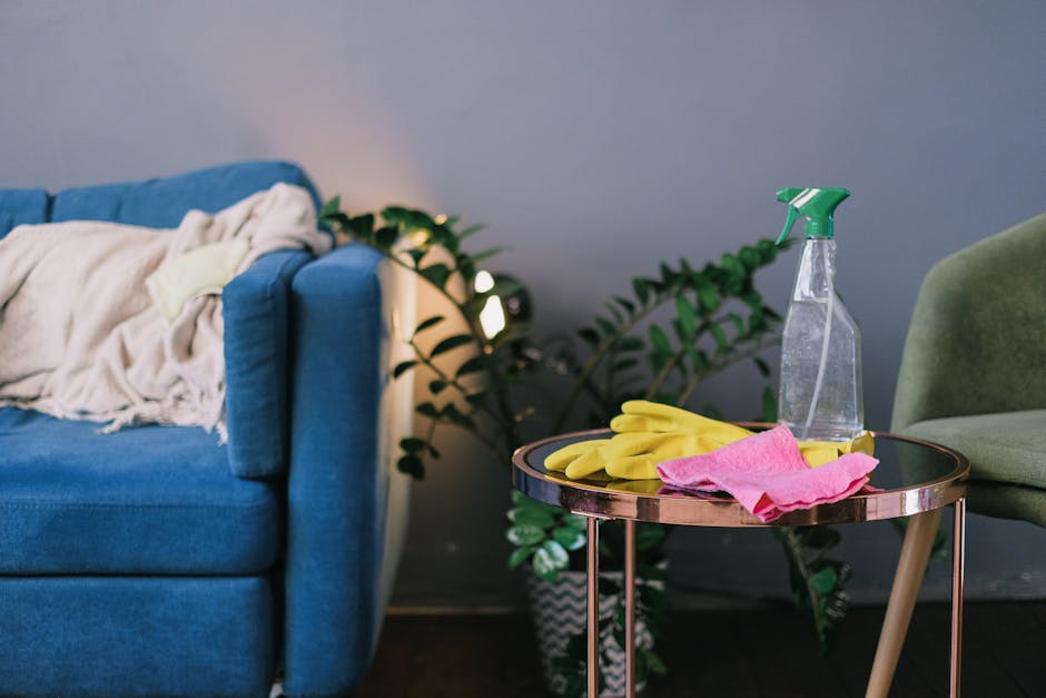 A beige fabric sofa situated in a bright, well-lit living room with white walls and decorative molding. The sofa appears clean and plush, with cushions neatly arranged. The surrounding area features a